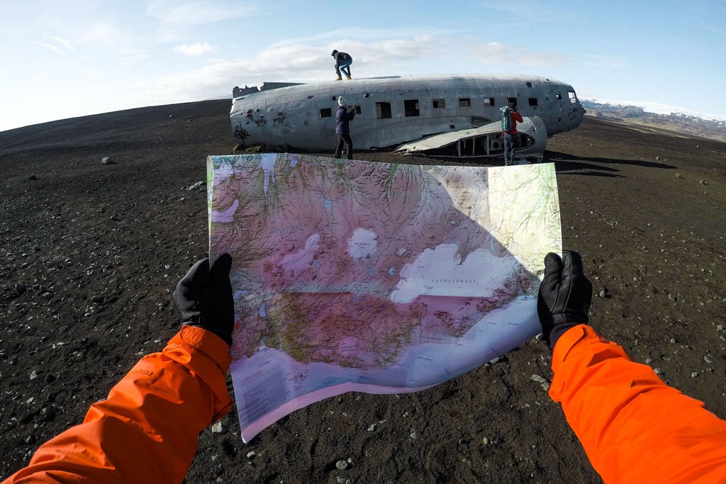 Person holding a nap of Iceland with a plane wreck in the background