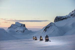 A group are snowmobiling on a glacier on a snowmobile tour in Iceland