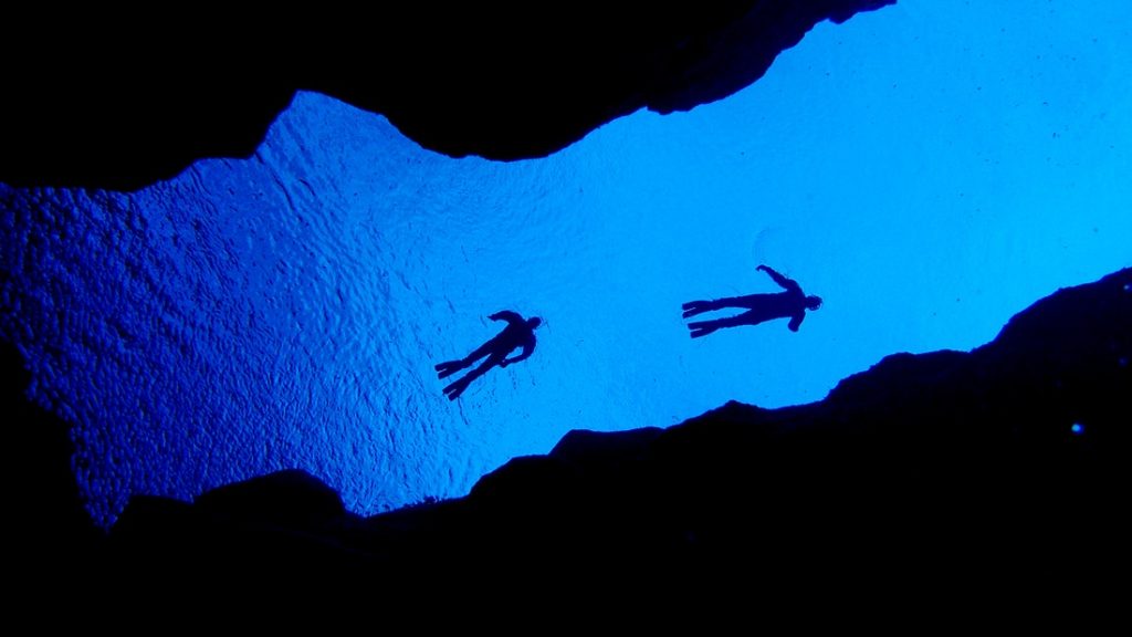 Two divers swim through the Silfra fissure in Iceland, their silhouettes vividly contrasted against the deep blue water, capturing a unique and luxurious underwater adventure.