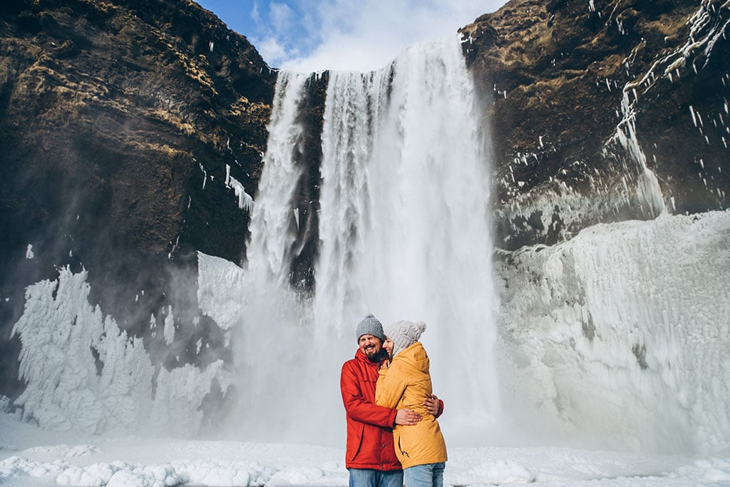 Couple hugging and posing in front of the Skogafoss waterfall in winter