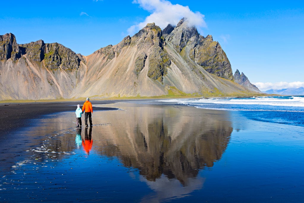 Parent and child standing on the beach looking at Stokksnes mountains in sunny weather