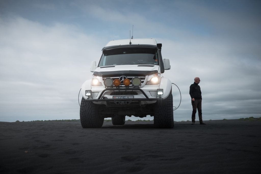 White monster truck parked on a stretch of black sand.