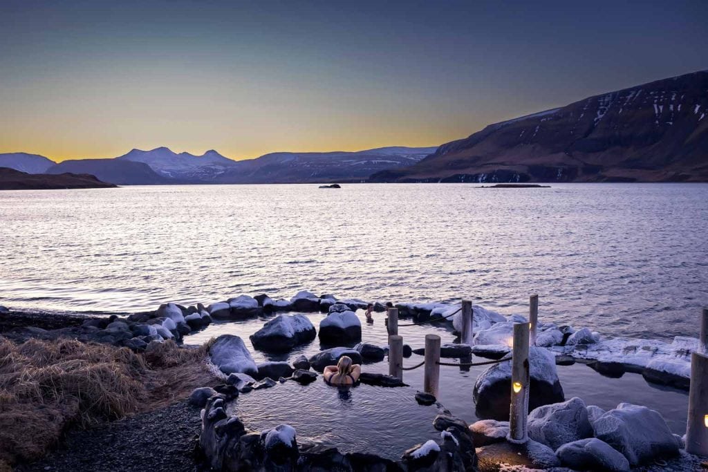 A woman relaxes in a steaming hot spring, gazing at a stunning sunset while encircled by a landscape of frost and ice. A woman relaxes in a steaming hot spring, gazing at a stunning sunset while encircled by a landscape of frost and ice.