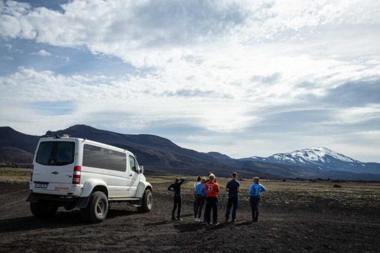 Group of tourists beside a superjeep with snow-capped mountains in the Iceland Highlands.