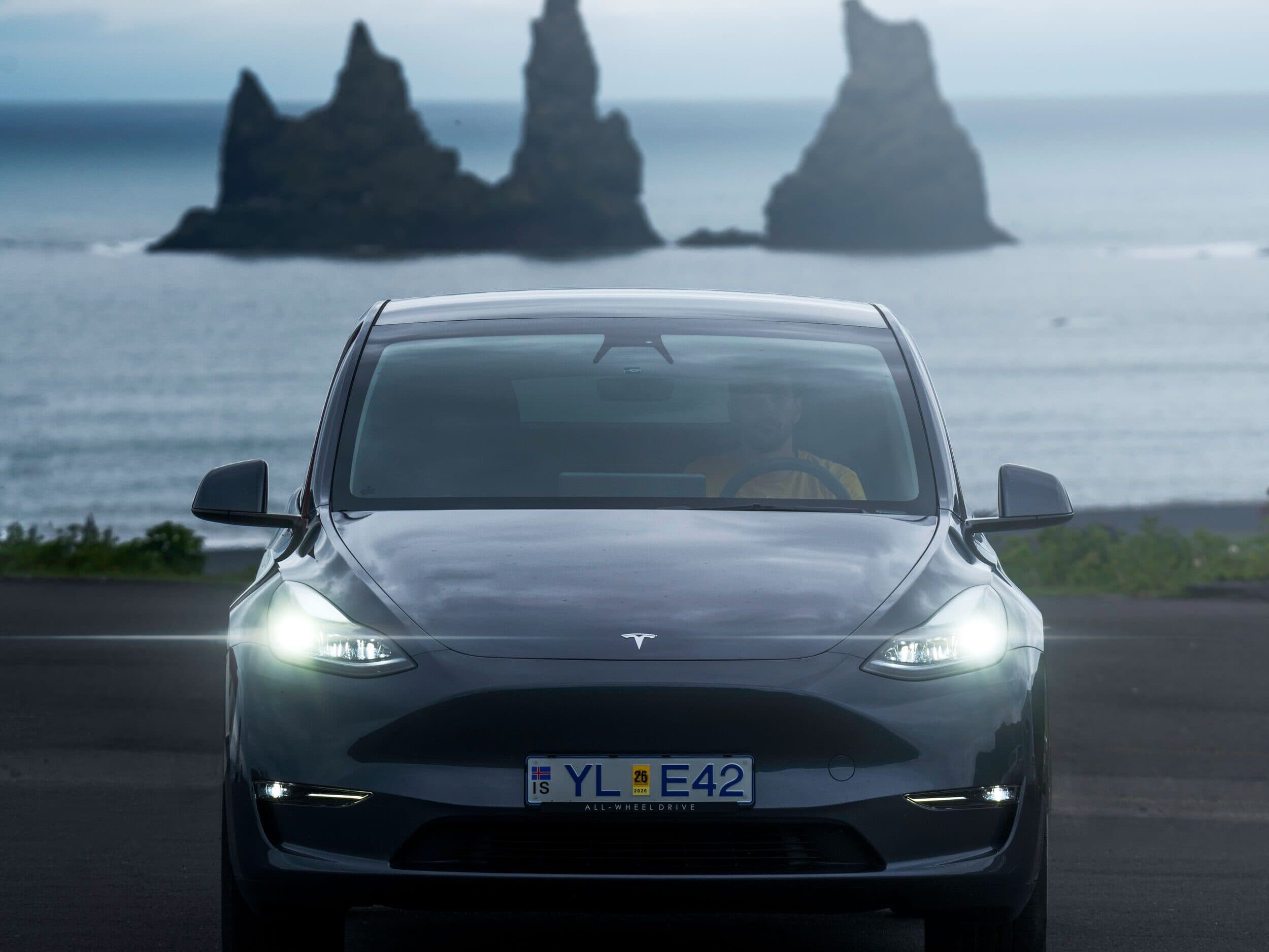 Tesla with Reynisdrangar Sea Stacks: A Tesla driving along the Icelandic coastline with the Reynisdrangar sea stacks in the background, symbolizing sustainable travel in breathtaking landscapes.