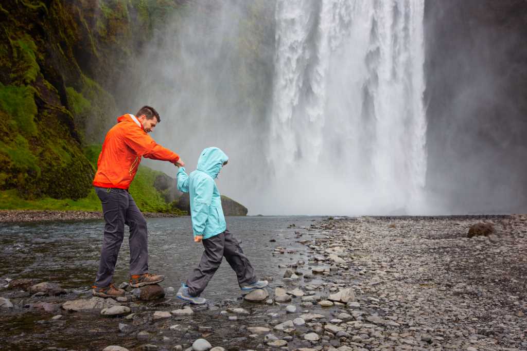 man and a kid in front of skógarfoss walking over river