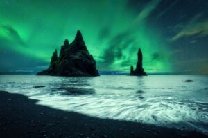 Green northern lights dancing over the cliffs of Reynisfjara