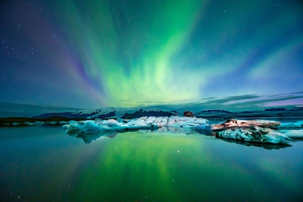 Northern lights in hues of green, blue and purple dancing in the night sky above a lake in Iceland in winter