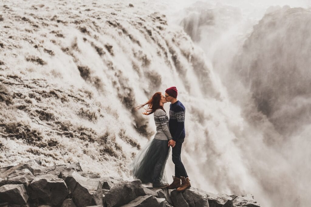 A couple leaning in for a kiss at a powerful waterfall in Iceland.
