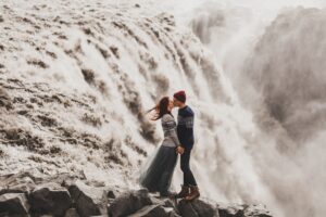 A couple leaning in for a kiss at a powerful waterfall in Iceland.