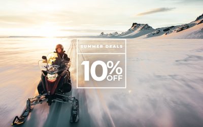 A person riding a snowmobile across a snowy landscape with mountains in the background at sunset. Text overlay: "Summer Deals 10% Off.