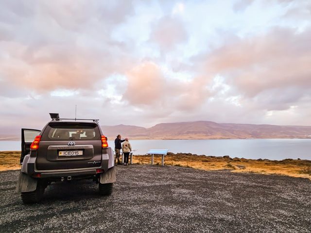 Off-road vehicle parked on a gravel road with scenic mountain and lake view at sunset.