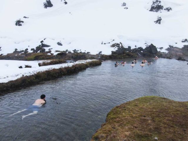 Tourists bathing in a hot spring in the snowy Iceland Highlands on a Landmannalaugar superjeep tour.