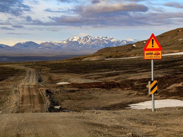 Dirt highland road with warning sign and distant peaks on the Iceland Highlands Super Jeep Tour.