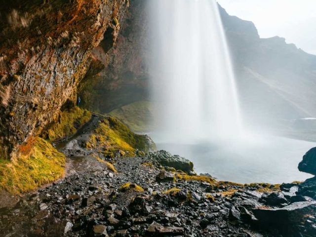 A majestic waterfall cascading from a rocky cliff surrounded by vibrant moss, with a misty spray at the base.