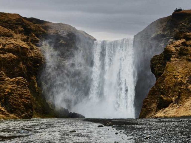 The powerful Skógafoss waterfall plunging down a rocky cliff, surrounded by mist and lush greenery in Iceland.