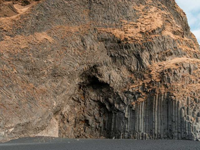 Close-up of basalt rock formations at the base of a cliff, showcasing the natural hexagonal columns formed by volcanic activity.