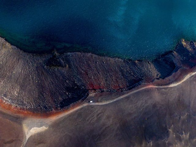 Aerial view of a vehicle driving along the edge of Ljótipollur crater lake, showcasing Iceland hidden gems.