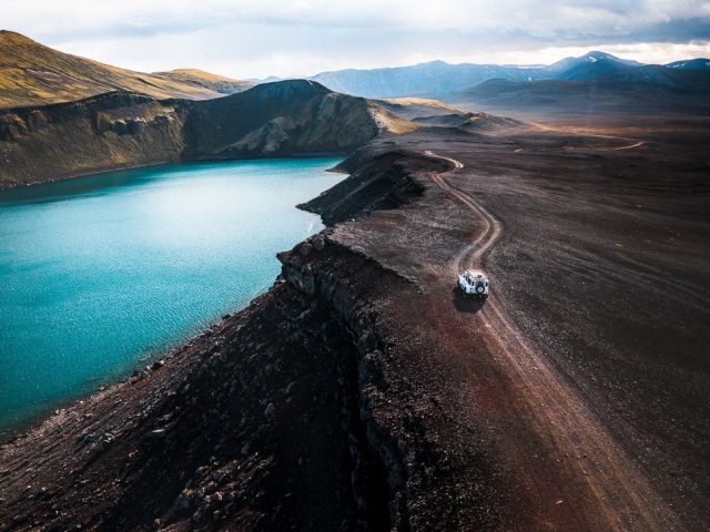 Off-road vehicle driving by the turquoise waters of Ljótipollur crater lake, showcasing Iceland private tours.