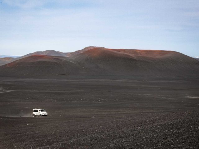 White superjeep driving through a vast, barren landscape in the Iceland Highlands on a Landmannalaugar tour.