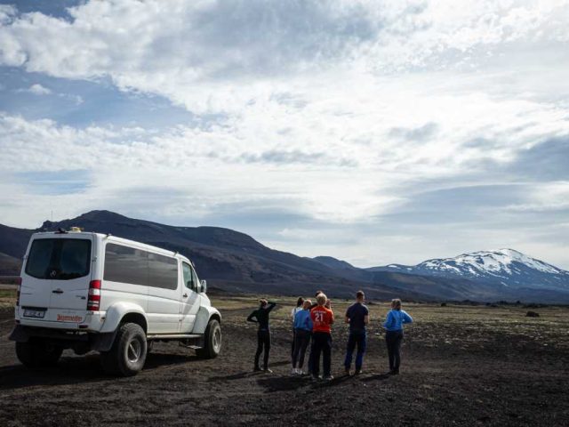 Group of tourists beside a superjeep with snow-capped mountains in the Iceland Highlands.