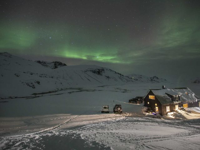 Camp setup with superjeeps under the Northern Lights in the snowy Iceland Highlands.