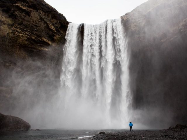 A person standing in front of Skogafoss waterfall