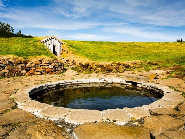 "Natural stone hot spring surrounded by green grass in Reykholt, Silver Circle, Iceland