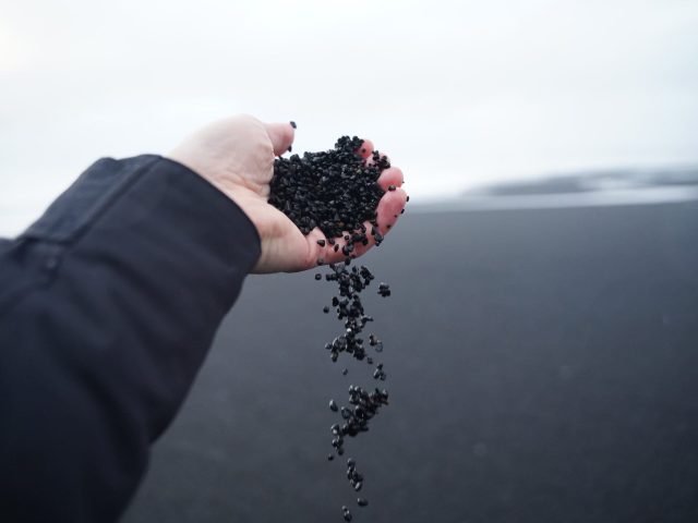 a hand fill of Black volcanic sand with the seacoast in the background