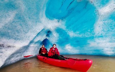 Two kayakers sitting in a red kayak under a blue ice cave in Iceland